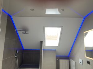 Kombination aus einer Lackspanndecke in der Farbe Beige und eine satin Spanndecke in der Farbe weiß mit umlaufender RGBWW LED-Beleuchtung und Einbaustrahlern.