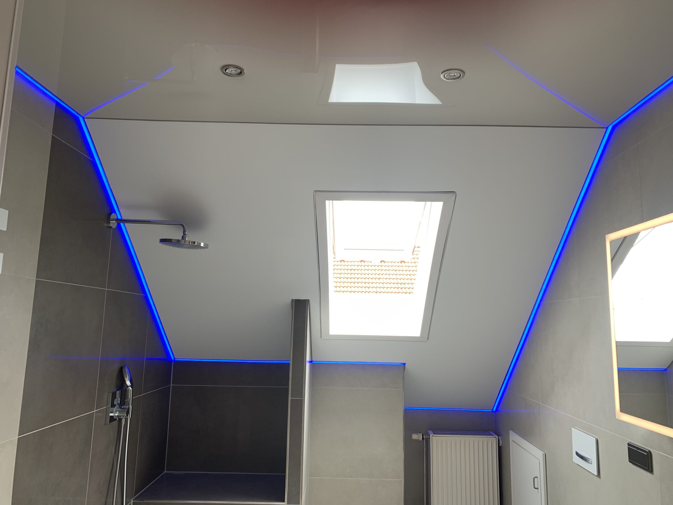 Kombination aus einer Lackspanndecke in der Farbe Beige und eine satin Spanndecke in der Farbe weiß mit umlaufender RGBWW LED-Beleuchtung und Einbaustrahlern.