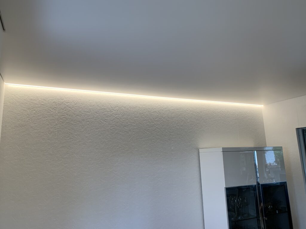 1_Satin_Spanndecke_Weiß_Indirekte_Beleuchtung_Warnweiß_Trebur Weiße Satin Spanndecke mit warmweißer LED-Beleuchtung auf zwei Seiten in einem Esszimmer