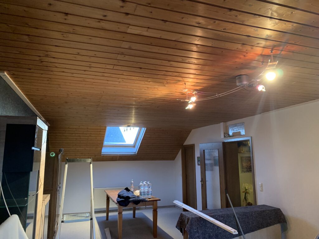 1_Vorher_OS_Holzdecke_Wohnzimmer_Trebur Decke vor Montage einer weißen Satin Spanndecke mit LED-Einbaustrahler in einem Ess- und Wohnzimmer mit Dachschräge in Trebur