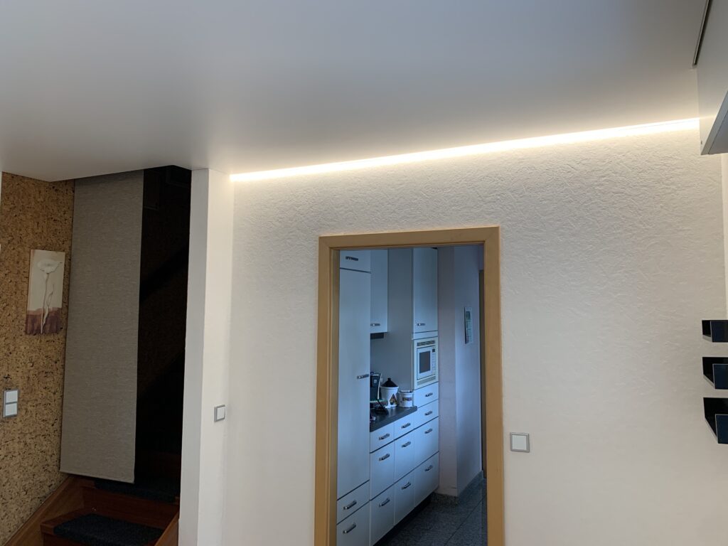 2_Satin_Spanndecke_Weiß_Indirekte_Beleuchtung_Warnweiß_Trebur Weiße Satin Spanndecke mit warmweißer LED-Beleuchtung auf zwei Seiten in einem Esszimmer
