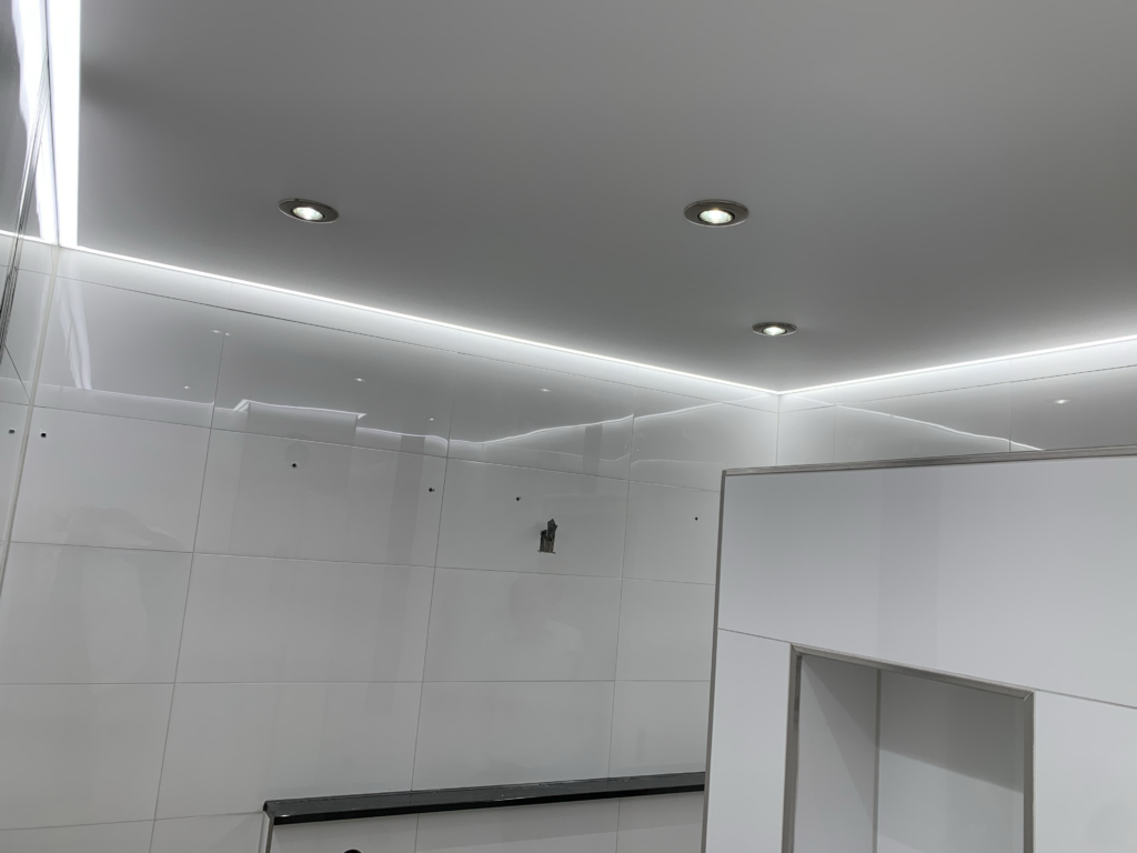 3_Lackspanndecke_LED_Einbaustrahler_LED_Beleuchtung_Bad_Rüsselsheim Weiße Lackspanndecke mit neutralweißer LED-Beleuchtung in der Schattenfuge und LED-Einbaustrahler in einem Bad in Bauschheim
