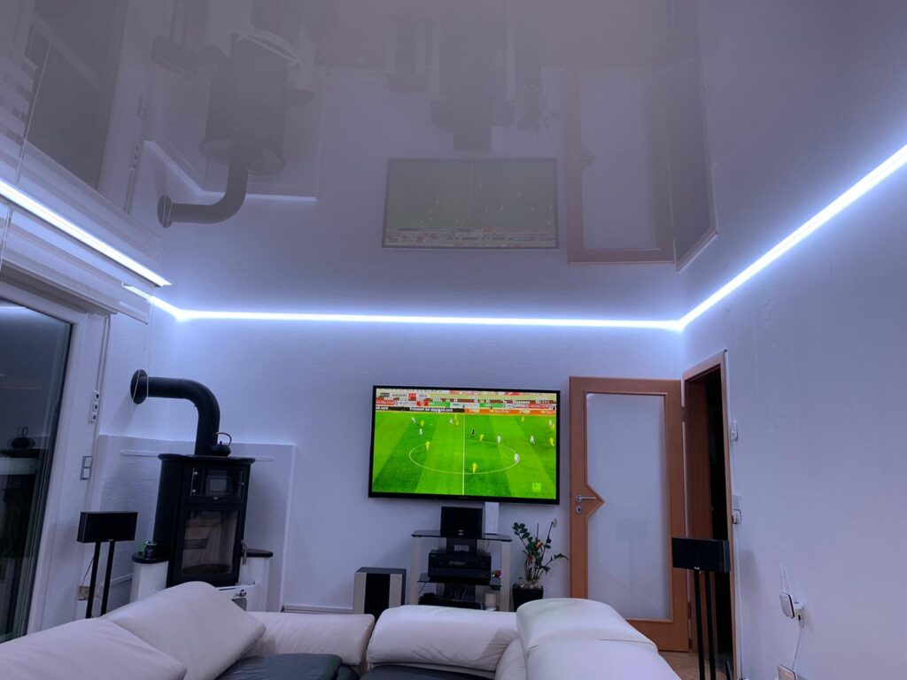 4_Lackspanndecke_Weiß_Indirekte_Beleuchtung_RGBW_Trebur Weiße Lackspanndecke mit RGBW LED-Beleuchtung in einem Wohnzimmer
