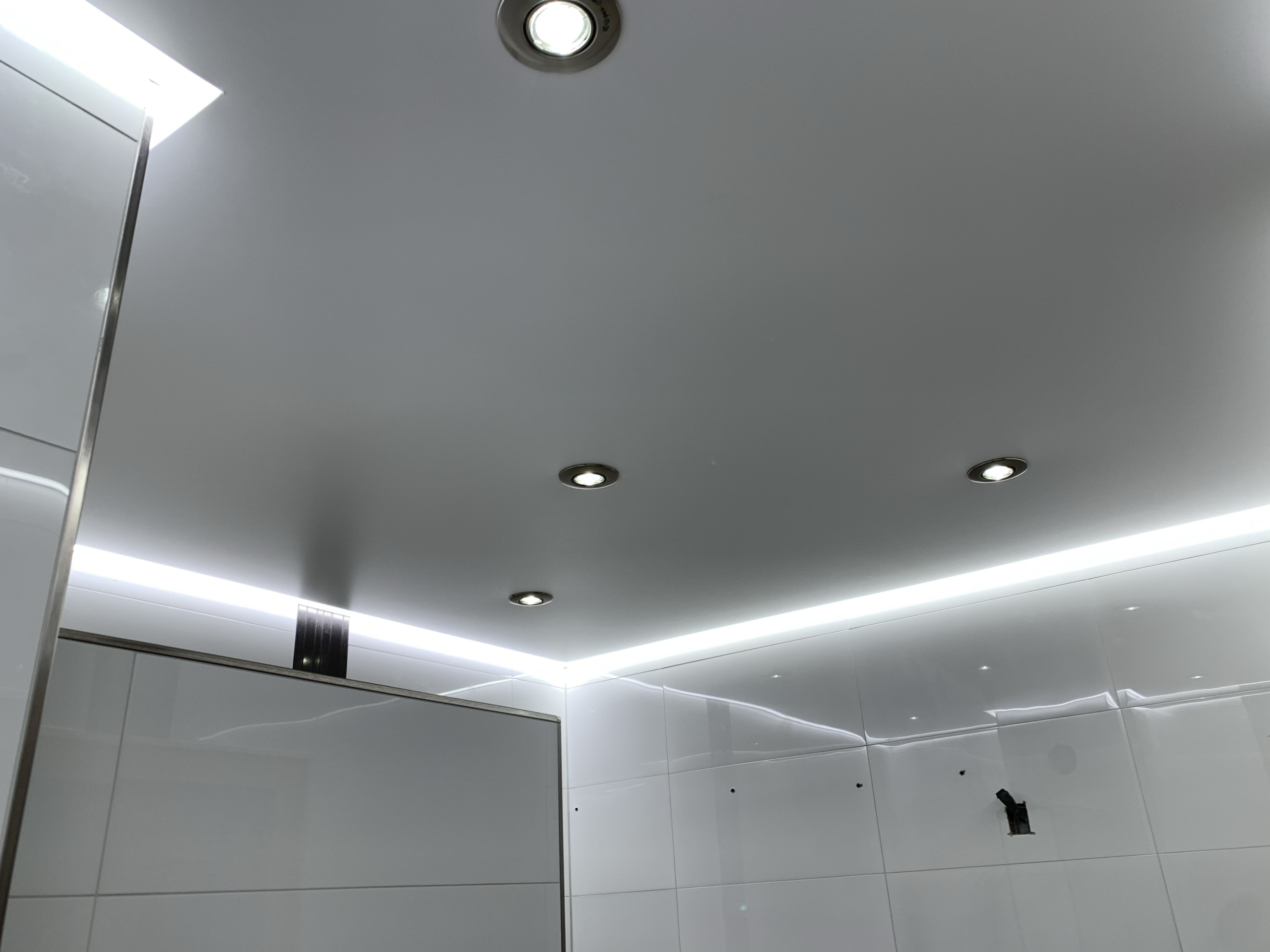 Weiße Lackspanndecke mit neutralweißer LED-Beleuchtung in der Schattenfuge und LED-Einbaustrahler in einem Bad in Bauschheim
