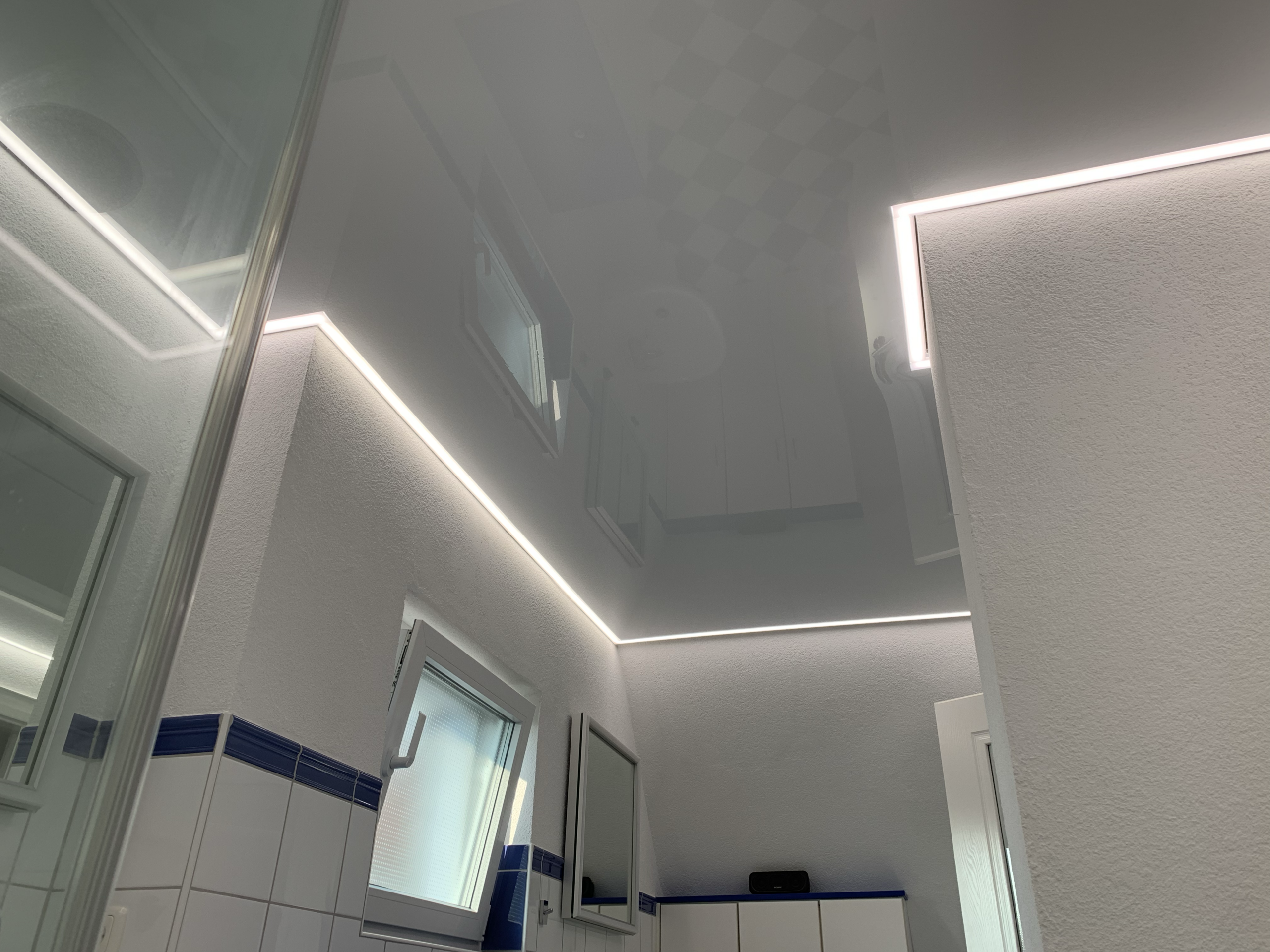 Weiße Lackspanndecke mit neutralweißer LED-Beleuchtung in der Schattenfuge in einem Bad